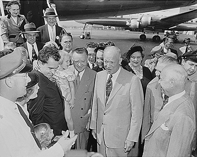 Nixon and Eisenhower stand with a crowd beside an airplane